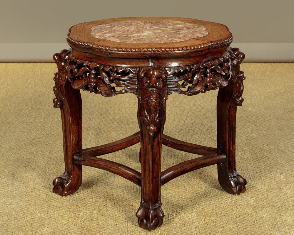 A low circular dark hardwood side table featuring an inset pink marble top, beaded rim, carved floral openwork apron, and claw feet.