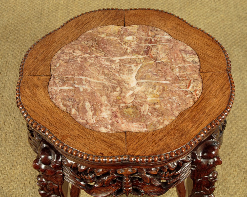 A low circular dark hardwood side table featuring an inset pink marble top, beaded rim, carved floral openwork apron, and claw feet. View III