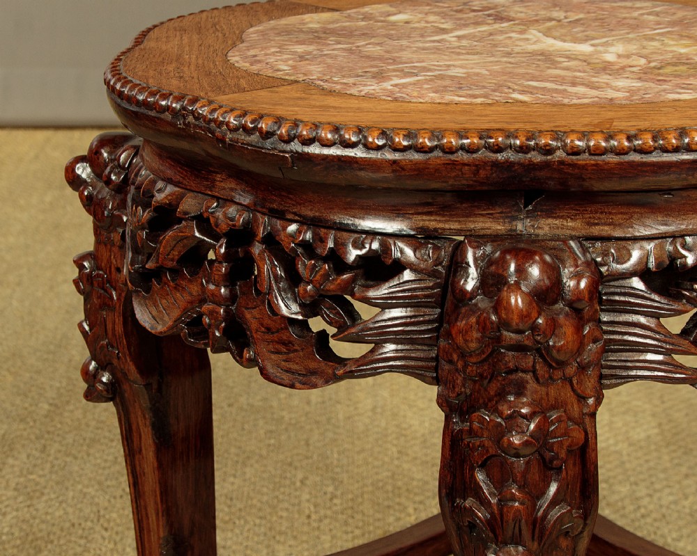 A low circular dark hardwood side table featuring an inset pink marble top, beaded rim, carved floral openwork apron, and claw feet. View VII