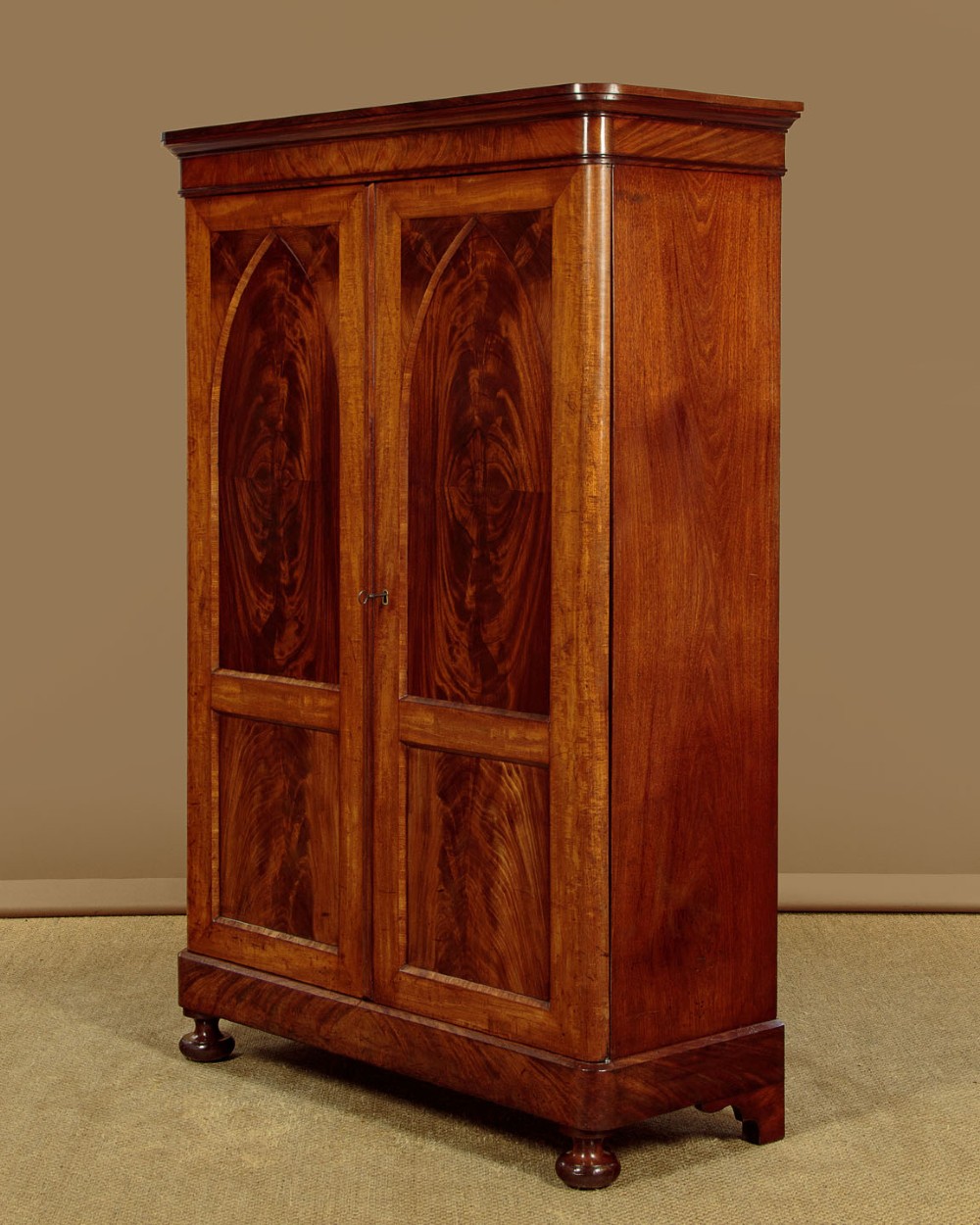 A mid-19th century compact Victorian mahogany wardrobe with flame mahogany arched door panels and round bun feet. View II
