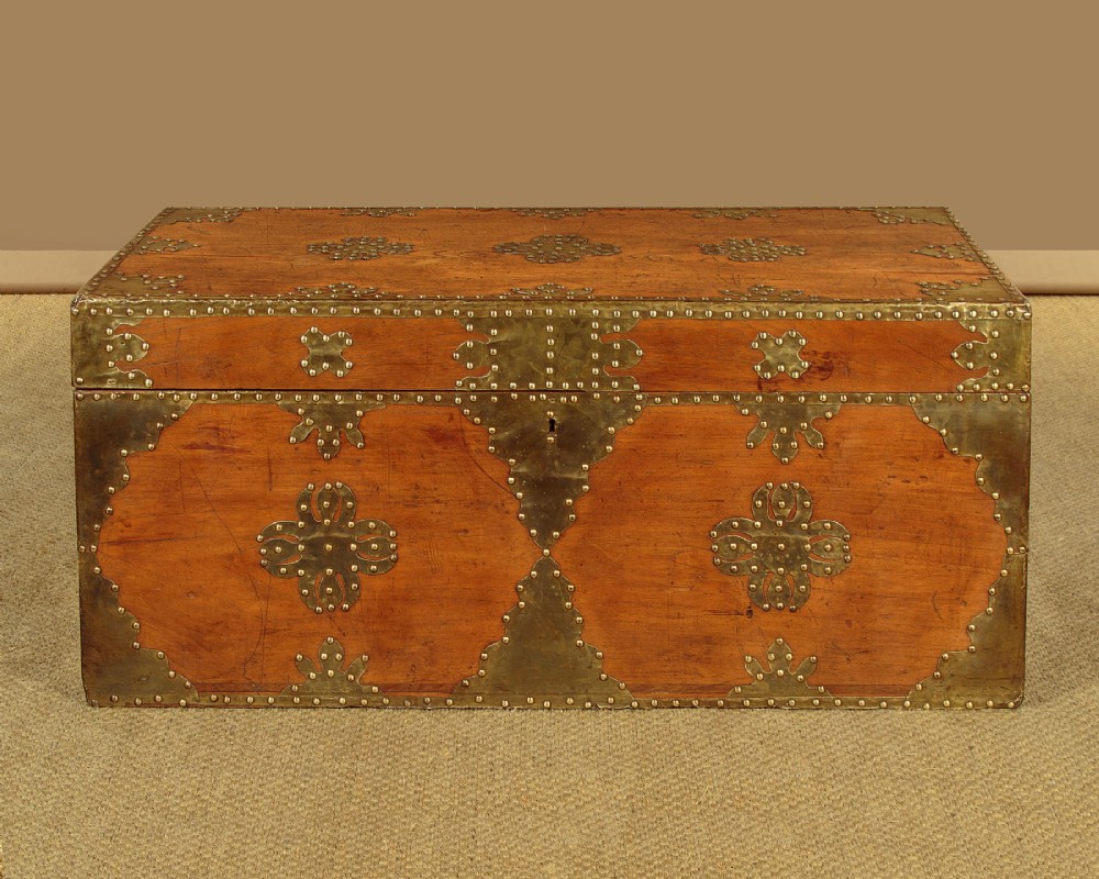 A rectangular warm brown wooden chest decorated with pierced brass corner brackets, floral mounts, and studded detailing across the top and front. View III