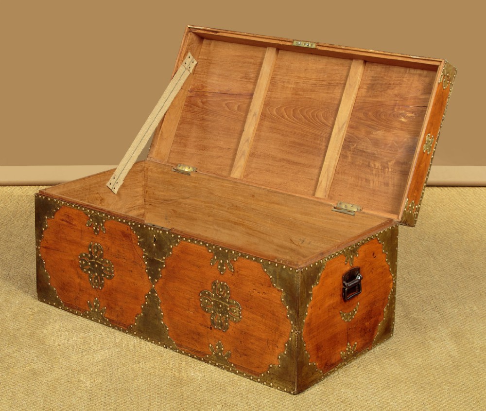 A rectangular warm brown wooden chest decorated with pierced brass corner brackets, floral mounts, and studded detailing across the top and front. View V