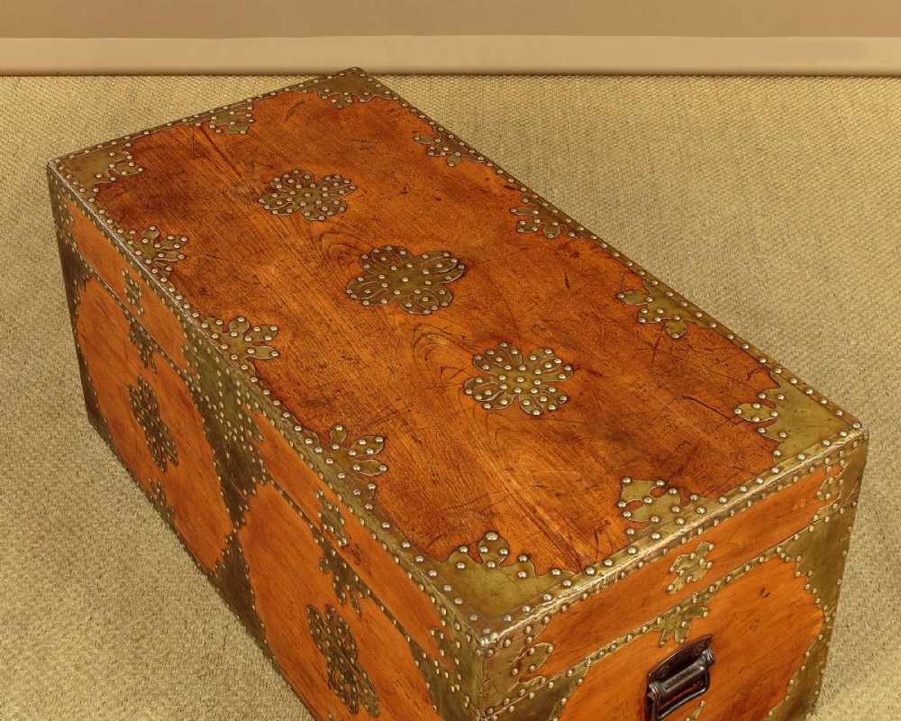 A rectangular warm brown wooden chest decorated with pierced brass corner brackets, floral mounts, and studded detailing across the top and front. View VI