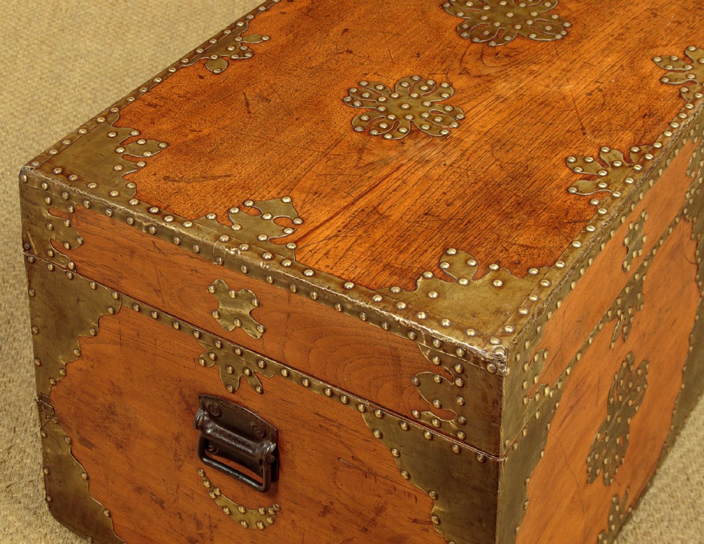 A rectangular warm brown wooden chest decorated with pierced brass corner brackets, floral mounts, and studded detailing across the top and front. View VII