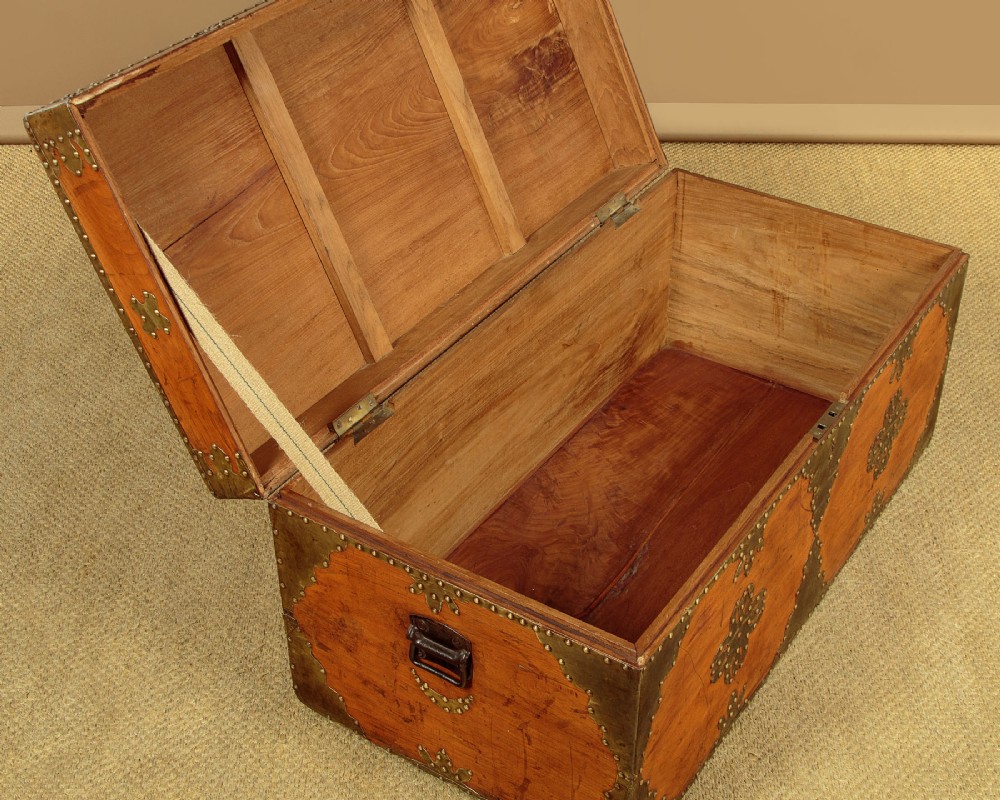 A rectangular warm brown wooden chest decorated with pierced brass corner brackets, floral mounts, and studded detailing across the top and front. View VIII