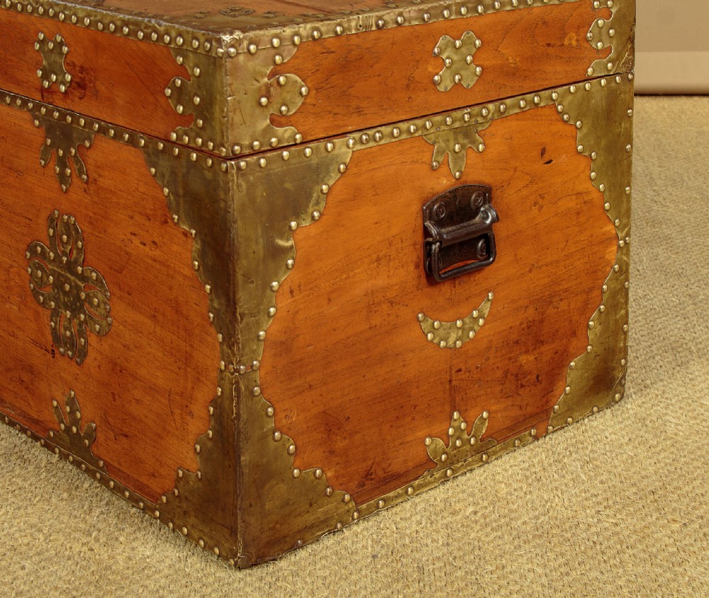 A rectangular warm brown wooden chest decorated with pierced brass corner brackets, floral mounts, and studded detailing across the top and front. View IX