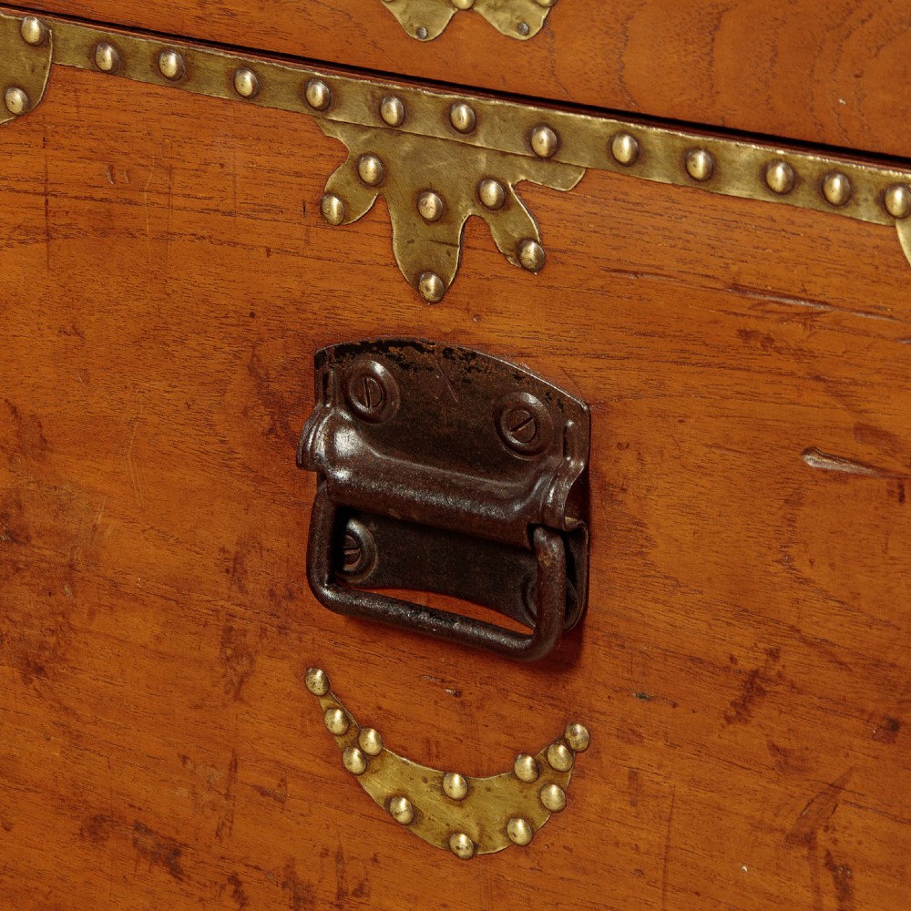 A rectangular warm brown wooden chest decorated with pierced brass corner brackets, floral mounts, and studded detailing across the top and front. View X