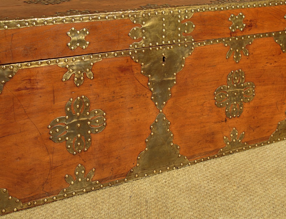 A rectangular warm brown wooden chest decorated with pierced brass corner brackets, floral mounts, and studded detailing across the top and front. View XI
