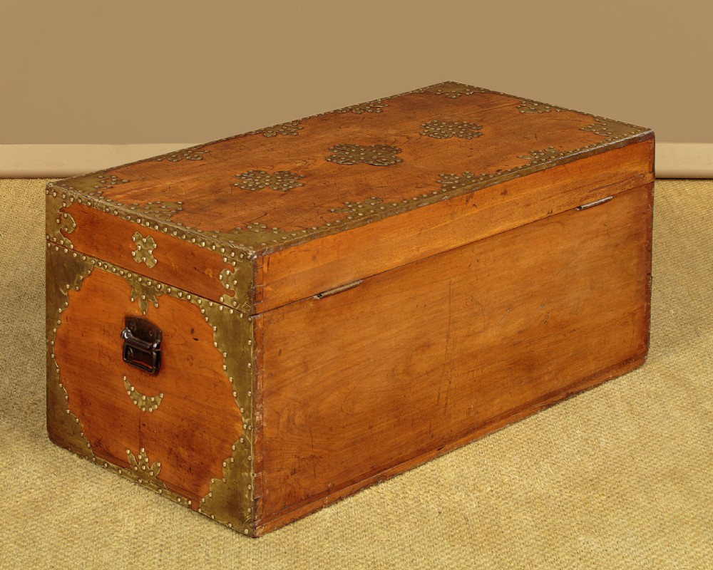 A rectangular warm brown wooden chest decorated with pierced brass corner brackets, floral mounts, and studded detailing across the top and front. View XII