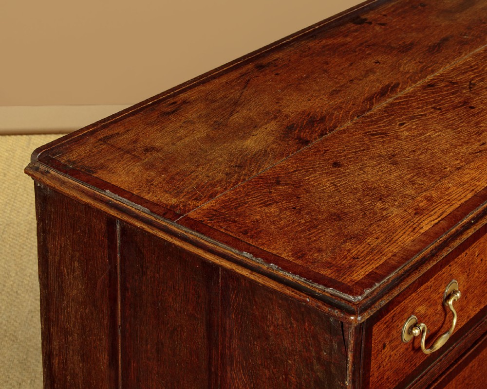 A long Georgian oak dresser base featuring multiple drawers with brass handles flanking a central double door cupboard, set on bracket feet. View VII