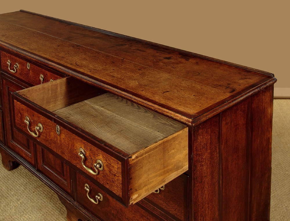 A long Georgian oak dresser base featuring multiple drawers with brass handles flanking a central double door cupboard, set on bracket feet. View VIII