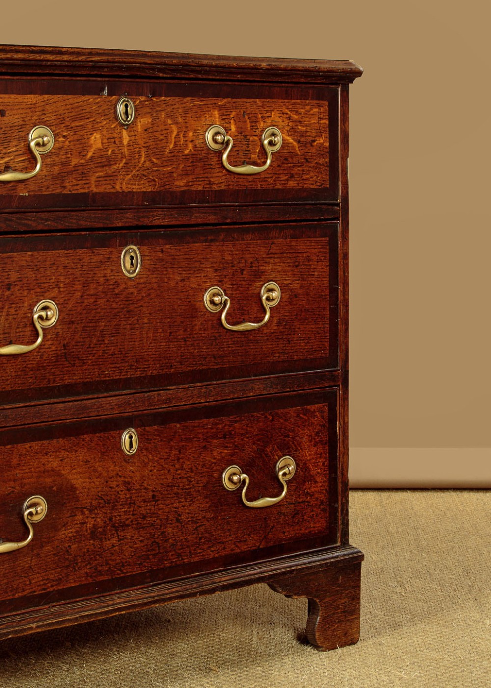 A long Georgian oak dresser base featuring multiple drawers with brass handles flanking a central double door cupboard, set on bracket feet. View IX