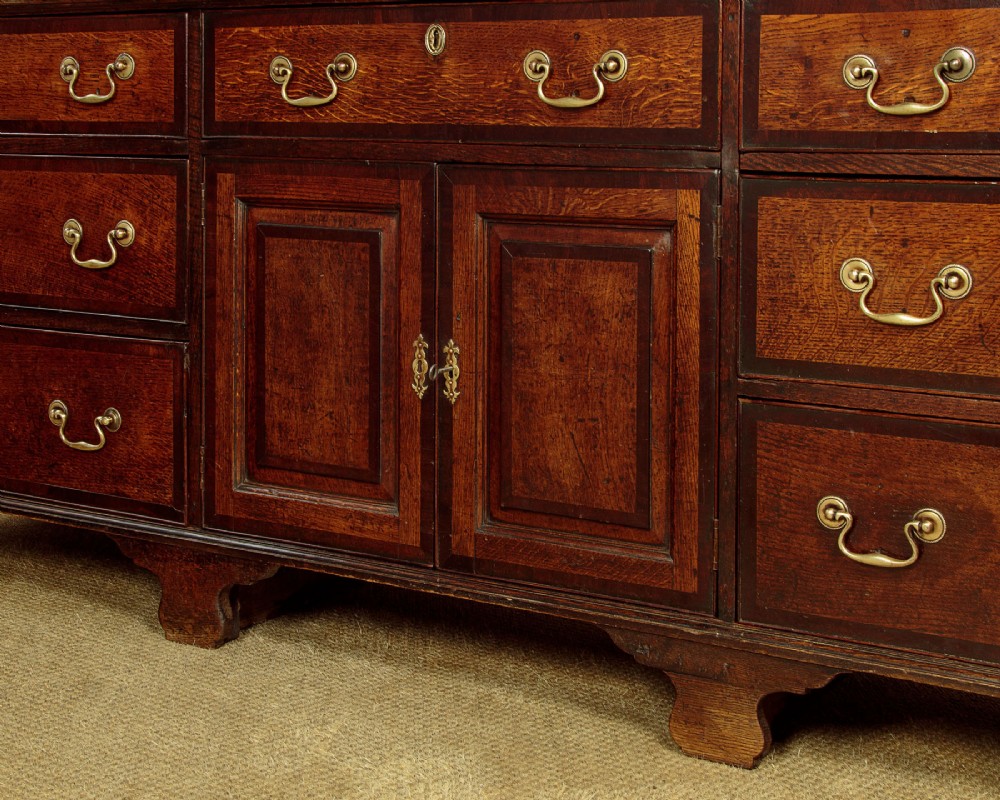 A long Georgian oak dresser base featuring multiple drawers with brass handles flanking a central double door cupboard, set on bracket feet. View XI