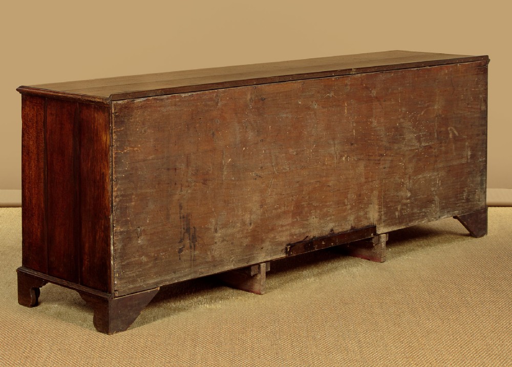 A long Georgian oak dresser base featuring multiple drawers with brass handles flanking a central double door cupboard, set on bracket feet. View XV