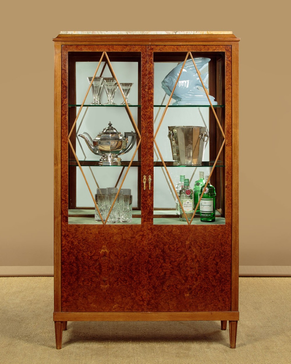 An Art Deco amboyna wood display cabinet featuring diamond-patterned glazing, glass shelves, a marble top, and tapered square legs. View II