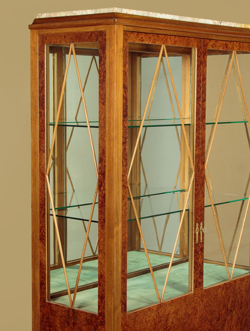 An Art Deco amboyna wood display cabinet featuring diamond-patterned glazing, glass shelves, a marble top, and tapered square legs. View VII