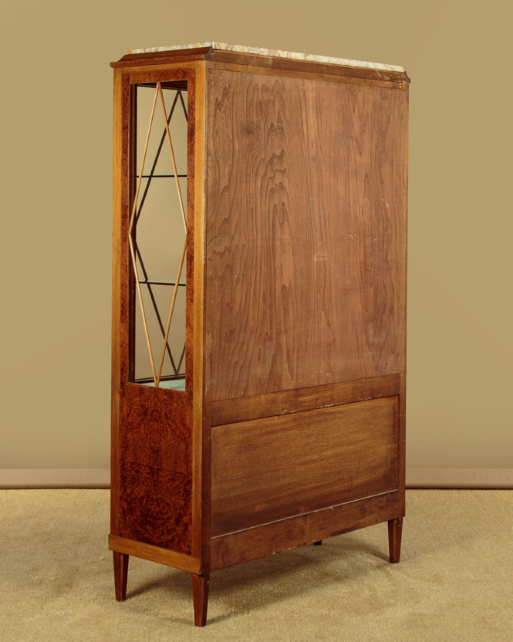 An Art Deco amboyna wood display cabinet featuring diamond-patterned glazing, glass shelves, a marble top, and tapered square legs. View X