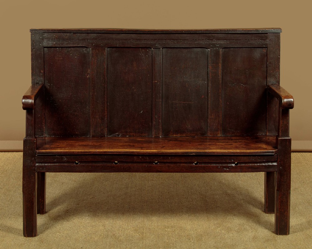 An 18th-century dark oak settle featuring a tall four-panel backrest, flat armrests, and a solid timber seat on straight legs. View II