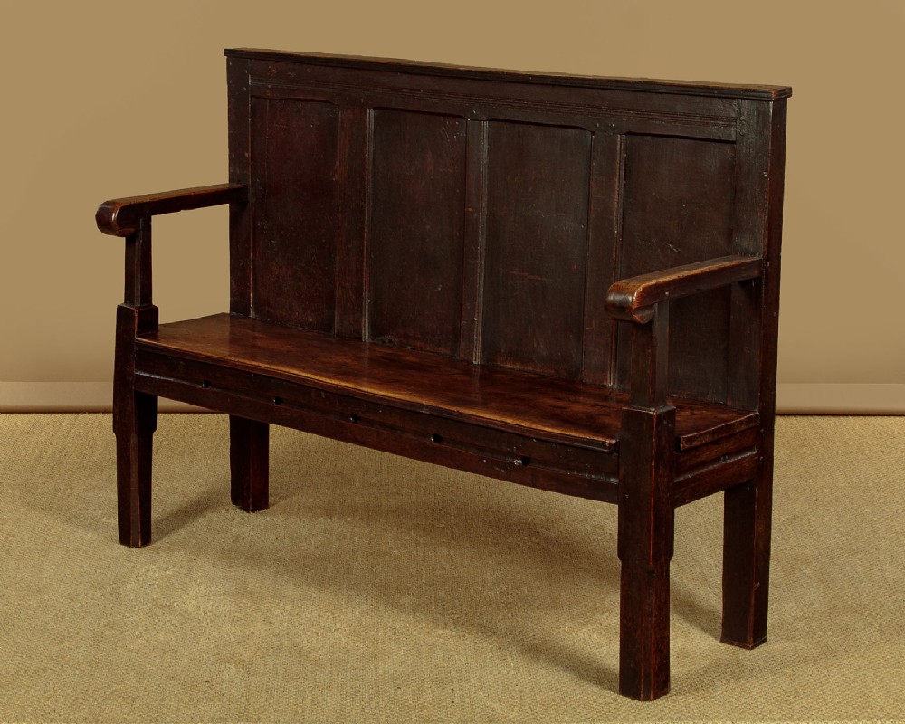 An 18th-century dark oak settle featuring a tall four-panel backrest, flat armrests, and a solid timber seat on straight legs. View III