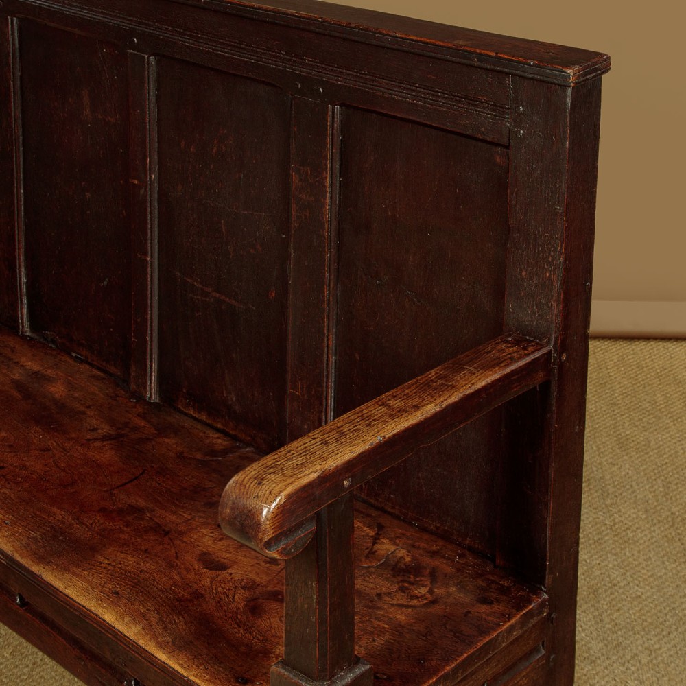 An 18th-century dark oak settle featuring a tall four-panel backrest, flat armrests, and a solid timber seat on straight legs. View VIII