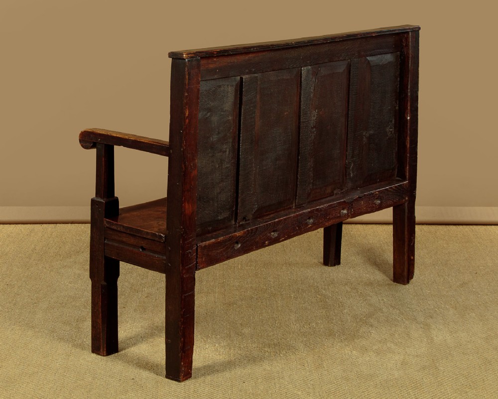 An 18th-century dark oak settle featuring a tall four-panel backrest, flat armrests, and a solid timber seat on straight legs. View XII