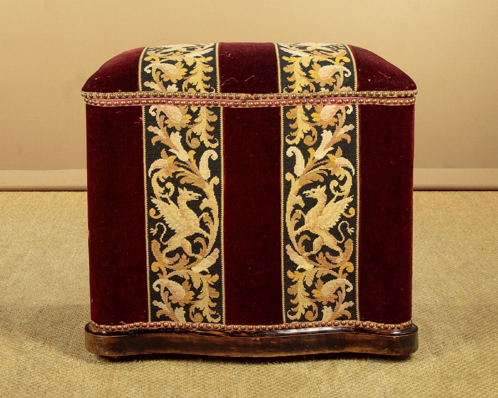 A late Victorian rectangular upholstered ottoman log box covered in deep burgundy velvet with two embroidered tapestry bands and brass stud trim, set on a dark wooden curved base. View II