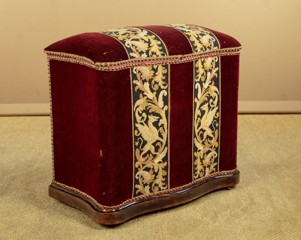A late Victorian rectangular upholstered ottoman log box covered in deep burgundy velvet with two embroidered tapestry bands and brass stud trim, set on a dark wooden curved base. View III