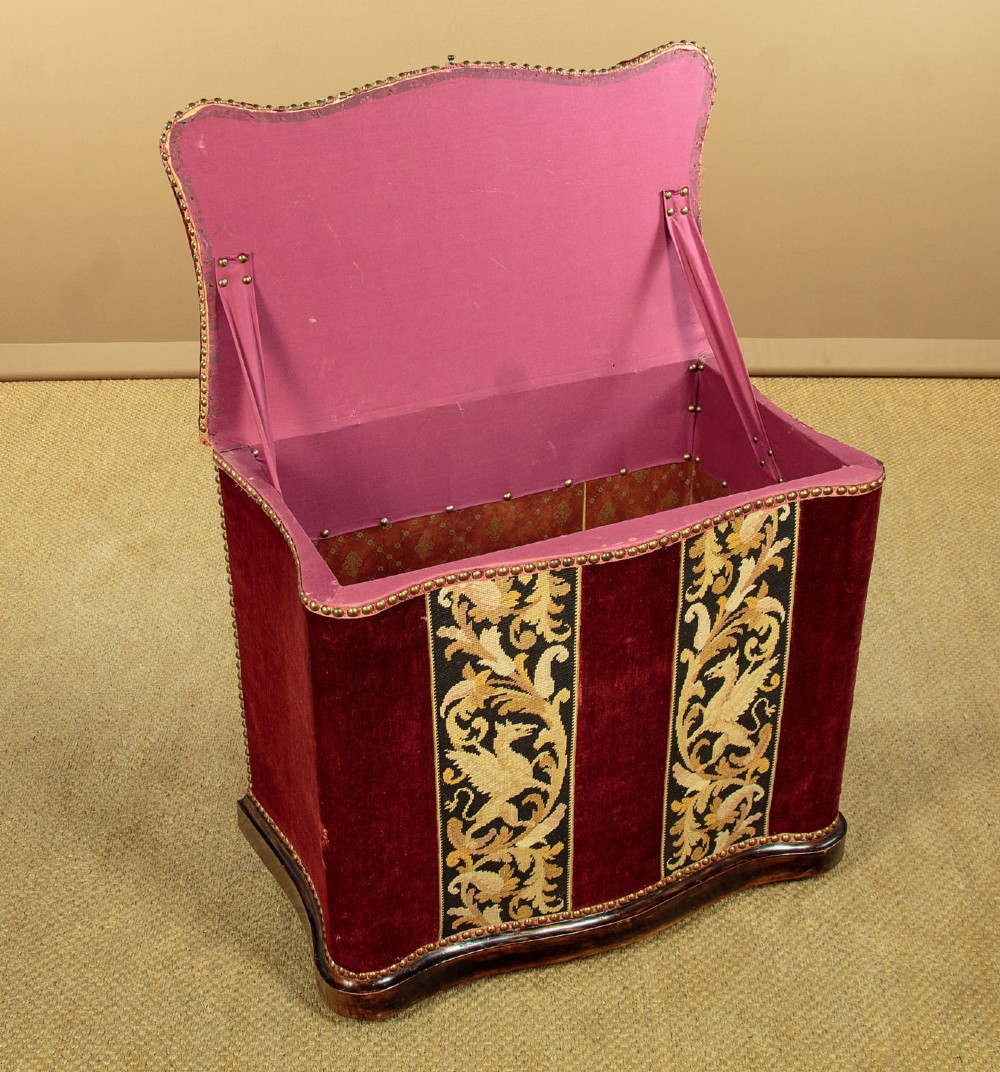 A late Victorian rectangular upholstered ottoman log box covered in deep burgundy velvet with two embroidered tapestry bands and brass stud trim, set on a dark wooden curved base. View IV
