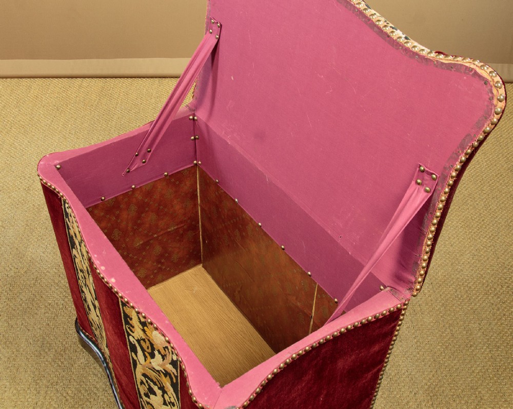 A late Victorian rectangular upholstered ottoman log box covered in deep burgundy velvet with two embroidered tapestry bands and brass stud trim, set on a dark wooden curved base. View VI