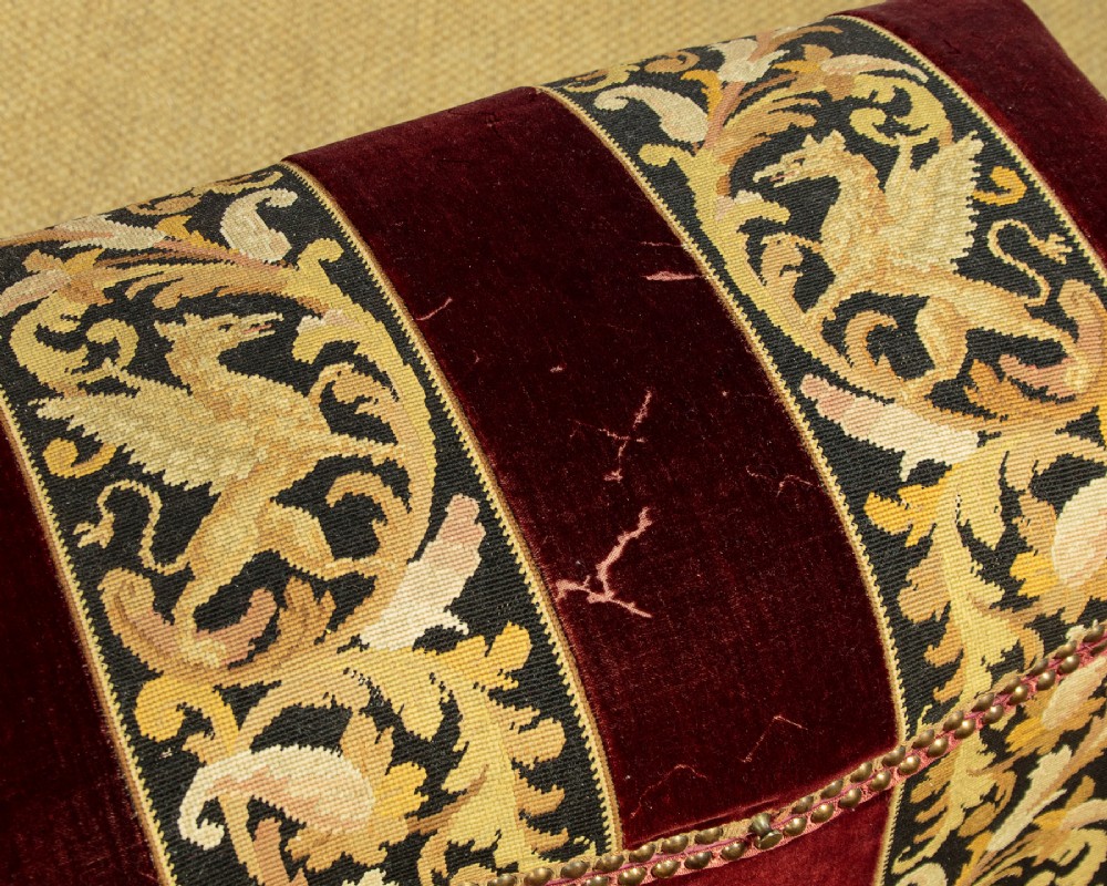 A late Victorian rectangular upholstered ottoman log box covered in deep burgundy velvet with two embroidered tapestry bands and brass stud trim, set on a dark wooden curved base. View VII