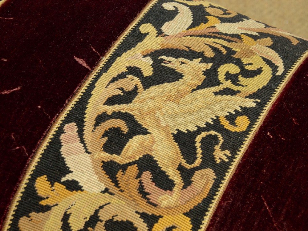 A late Victorian rectangular upholstered ottoman log box covered in deep burgundy velvet with two embroidered tapestry bands and brass stud trim, set on a dark wooden curved base. View VIII