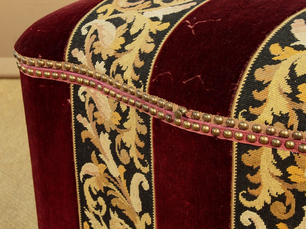 A late Victorian rectangular upholstered ottoman log box covered in deep burgundy velvet with two embroidered tapestry bands and brass stud trim, set on a dark wooden curved base. View X