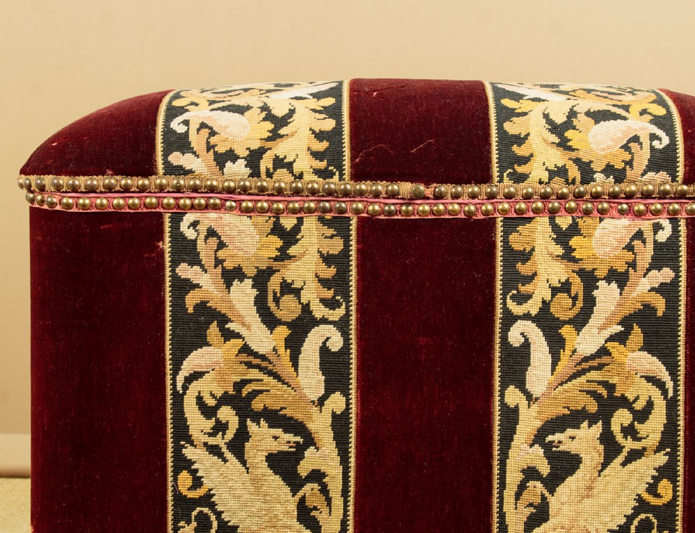 A late Victorian rectangular upholstered ottoman log box covered in deep burgundy velvet with two embroidered tapestry bands and brass stud trim, set on a dark wooden curved base. View XI