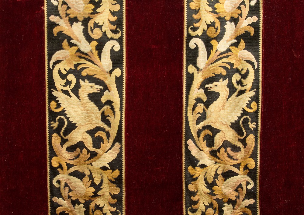 A late Victorian rectangular upholstered ottoman log box covered in deep burgundy velvet with two embroidered tapestry bands and brass stud trim, set on a dark wooden curved base. View XII