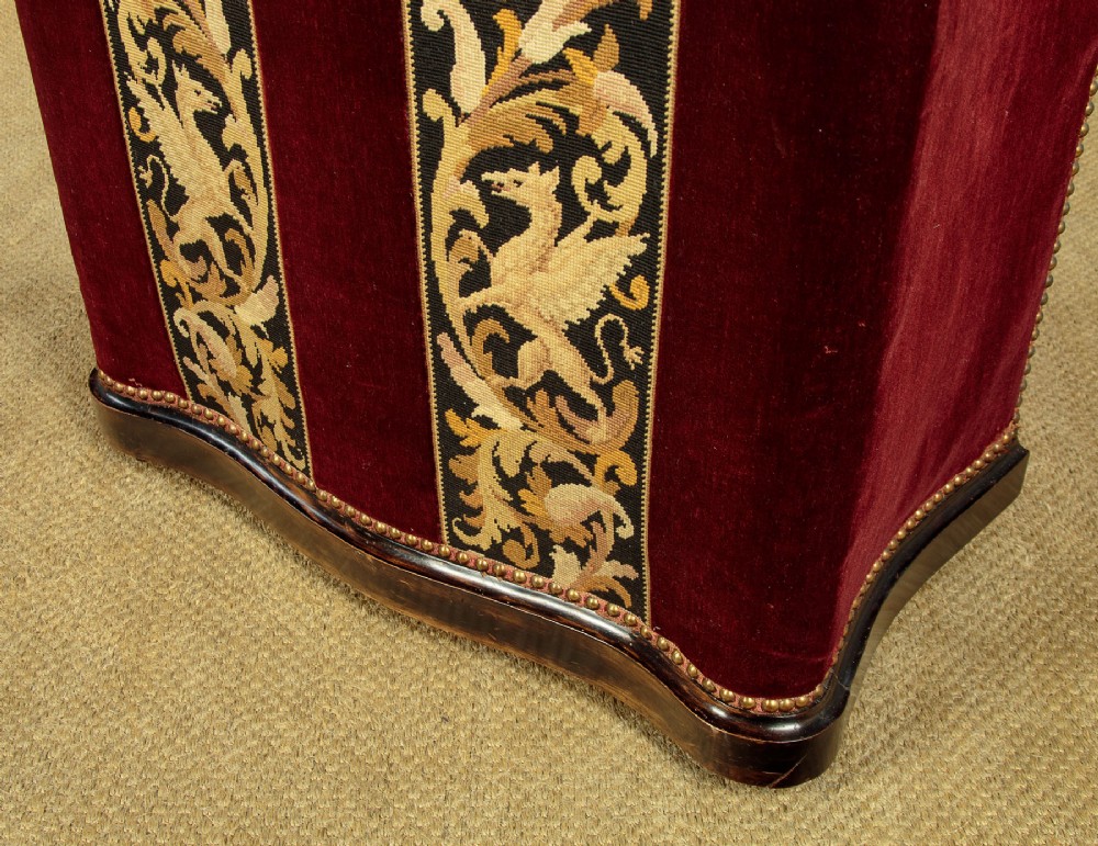 A late Victorian rectangular upholstered ottoman log box covered in deep burgundy velvet with two embroidered tapestry bands and brass stud trim, set on a dark wooden curved base. View XIII