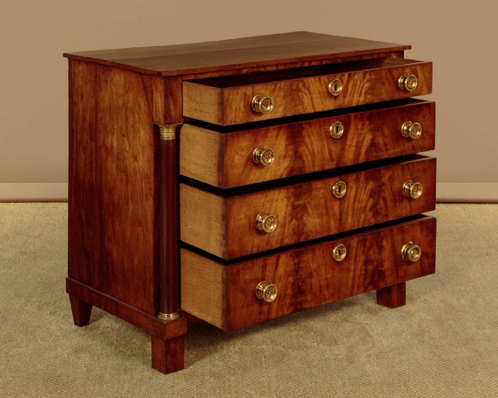 A small 19th-century Empire style mahogany chest featuring four drawers with flame veneer finishes, brass knob handles, keyhole escutcheons, and flank columns. View IV