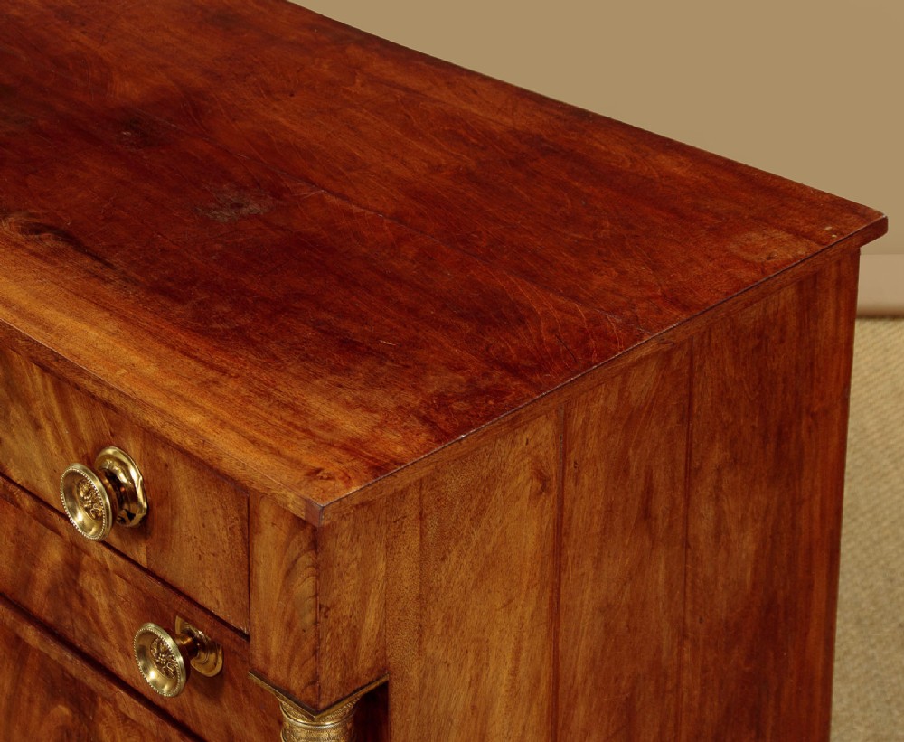 A small 19th-century Empire style mahogany chest featuring four drawers with flame veneer finishes, brass knob handles, keyhole escutcheons, and flank columns. View VI