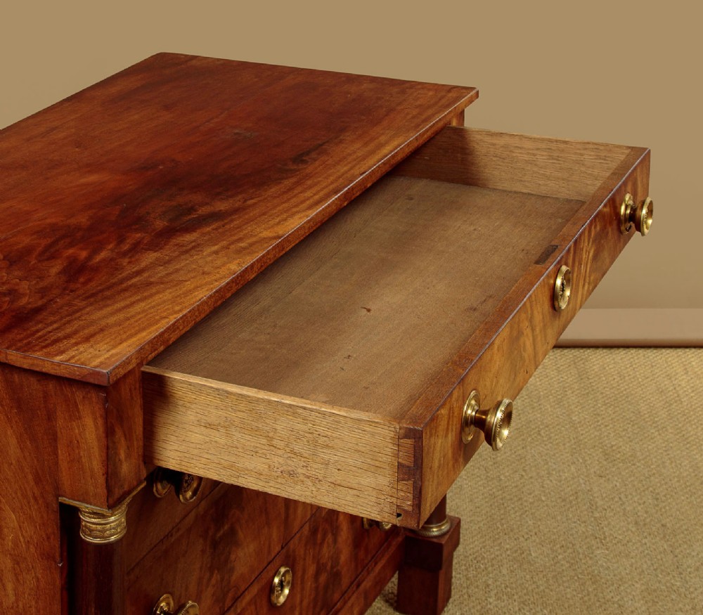 A small 19th-century Empire style mahogany chest featuring four drawers with flame veneer finishes, brass knob handles, keyhole escutcheons, and flank columns. View VII