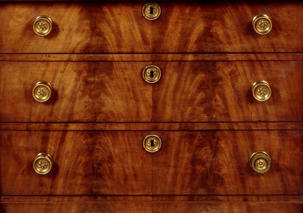 A small 19th-century Empire style mahogany chest featuring four drawers with flame veneer finishes, brass knob handles, keyhole escutcheons, and flank columns. View VIII