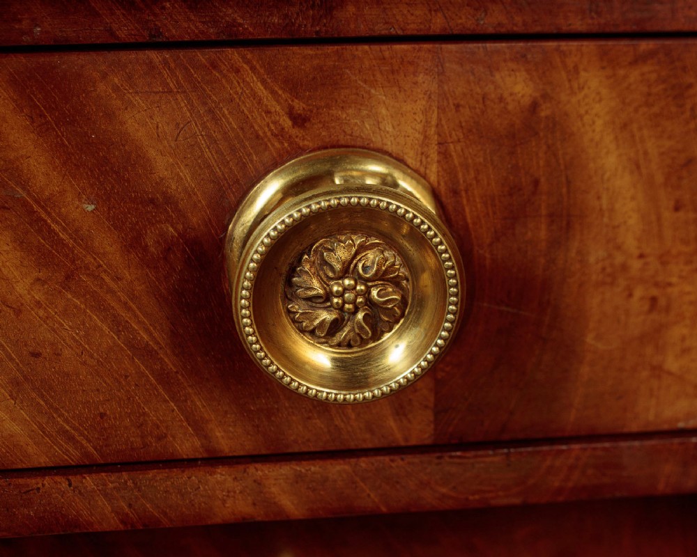 A small 19th-century Empire style mahogany chest featuring four drawers with flame veneer finishes, brass knob handles, keyhole escutcheons, and flank columns. View XI