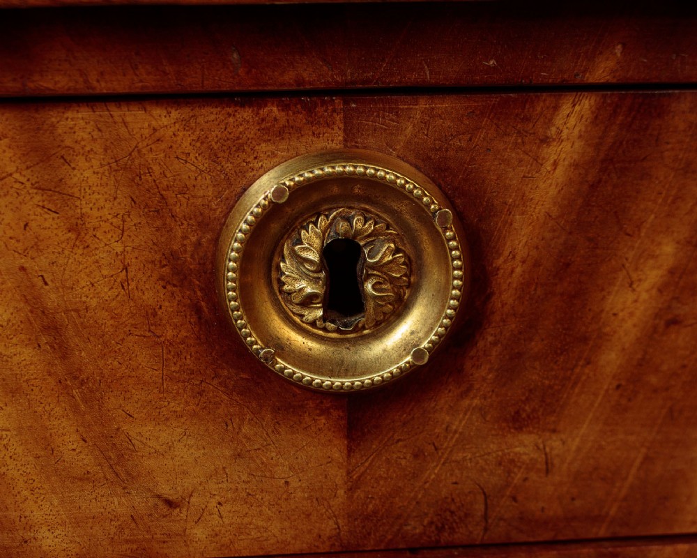 A small 19th-century Empire style mahogany chest featuring four drawers with flame veneer finishes, brass knob handles, keyhole escutcheons, and flank columns. View XII