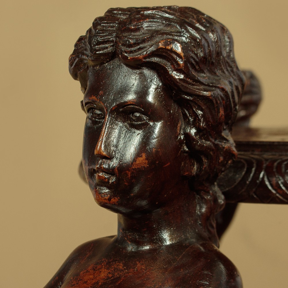 A dark carved wooden pedestal stand featuring three figurative sculpted supports on a tripartite base supporting a circular carved top. View VIII