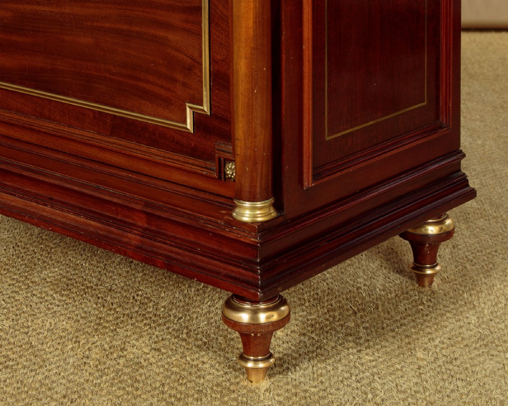 A tall, narrow mahogany bookcase featuring a single glazed door, internal wooden shelves, brass fluted column accents, and a brass gallery top. View XII