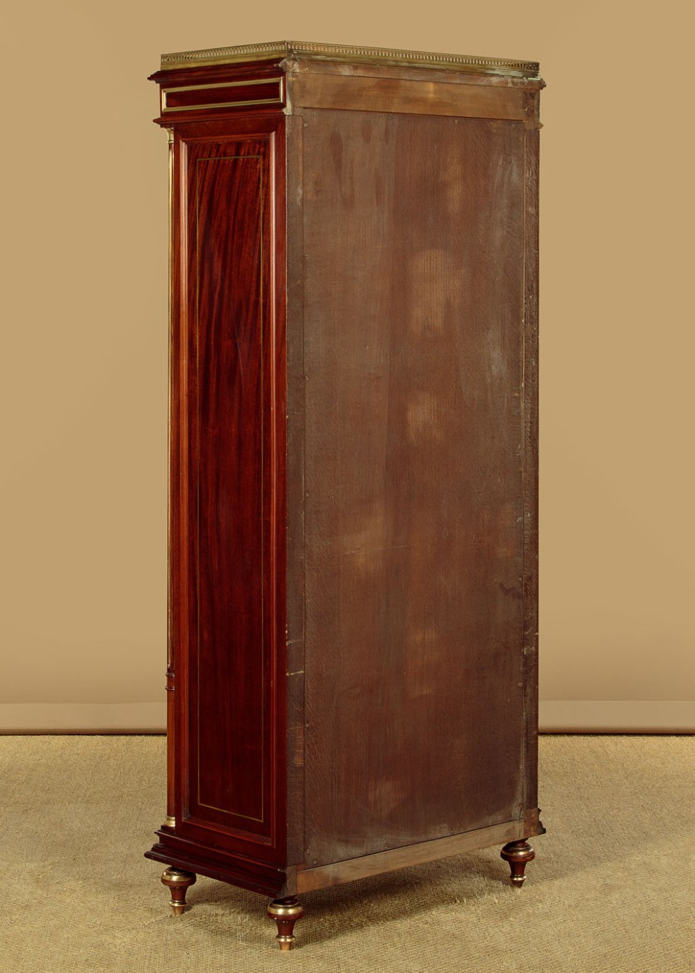 A tall, narrow mahogany bookcase featuring a single glazed door, internal wooden shelves, brass fluted column accents, and a brass gallery top. View XIII