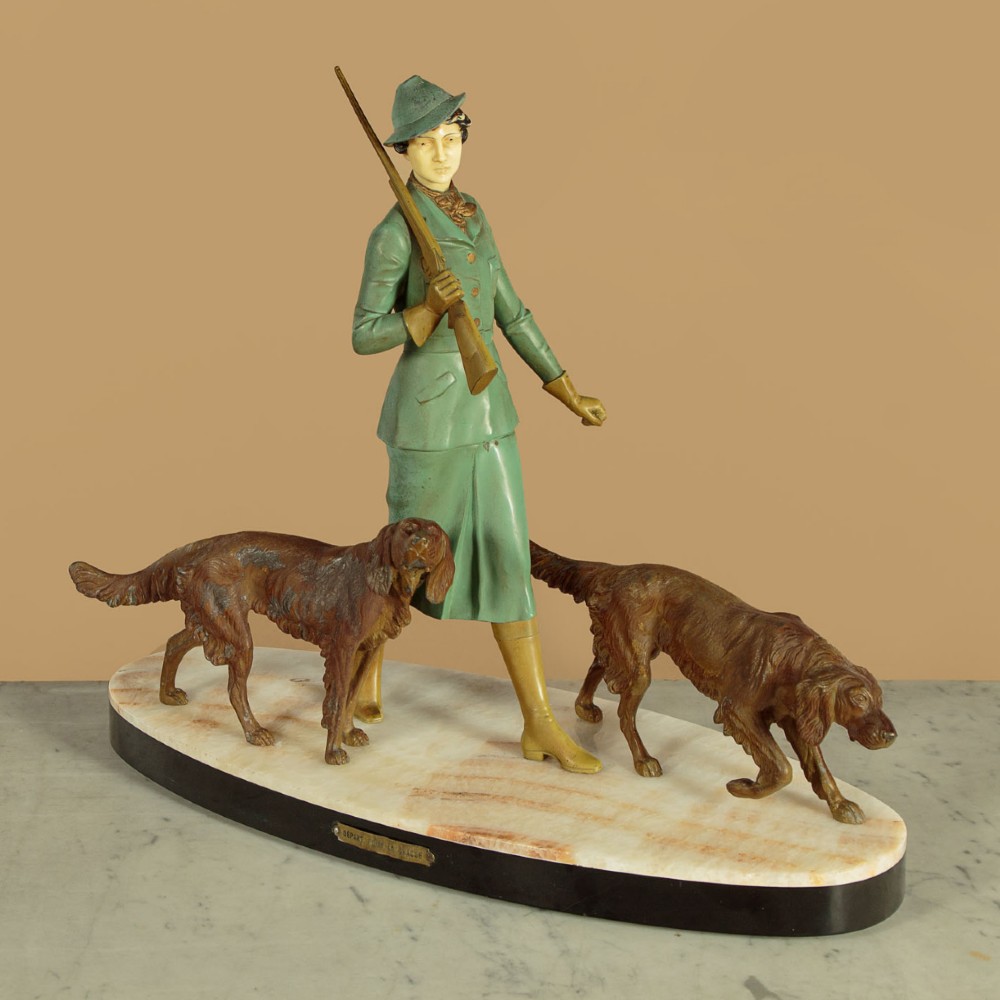Art Deco figure group depicting a huntress in a green suit with two hunting dogs mounted on an oval marble base.