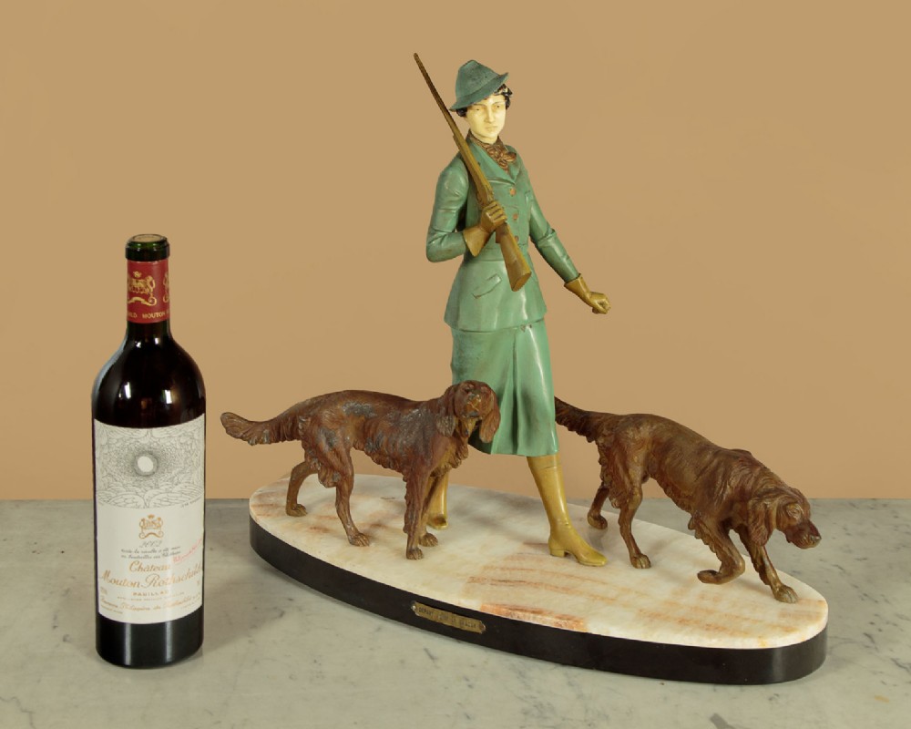 Art Deco figure group depicting a huntress in a green suit with two hunting dogs mounted on an oval marble base. View II
