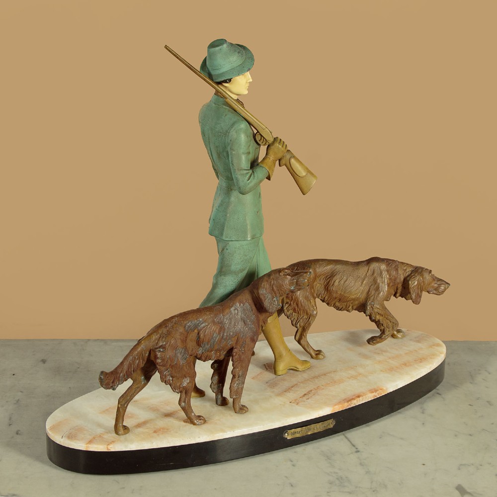 Art Deco figure group depicting a huntress in a green suit with two hunting dogs mounted on an oval marble base. View IV
