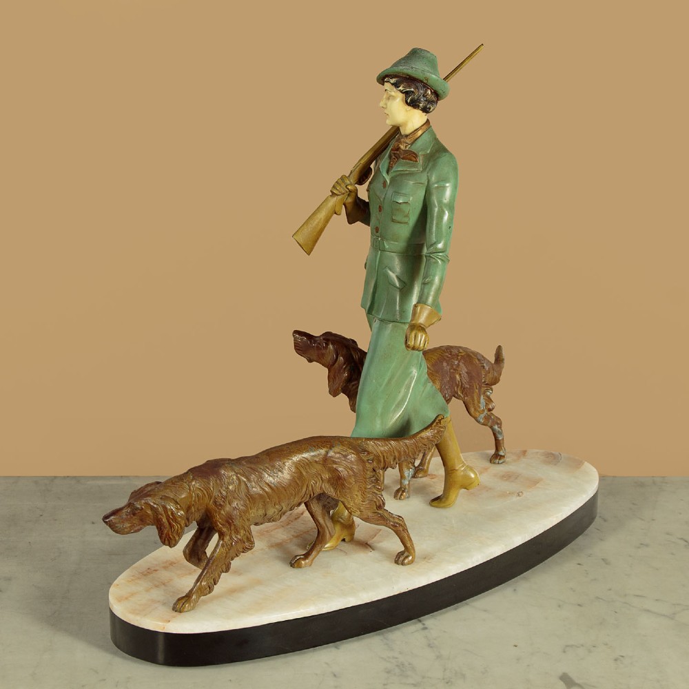 Art Deco figure group depicting a huntress in a green suit with two hunting dogs mounted on an oval marble base. View V
