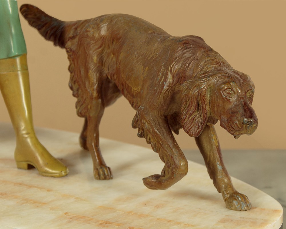 Art Deco figure group depicting a huntress in a green suit with two hunting dogs mounted on an oval marble base. View X