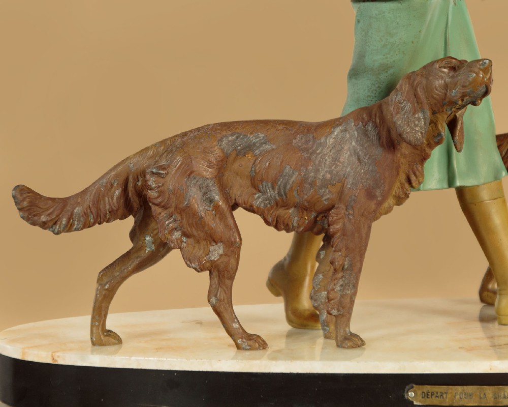 Art Deco figure group depicting a huntress in a green suit with two hunting dogs mounted on an oval marble base. View XI